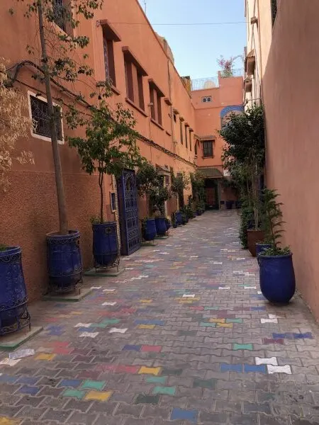 Ruelle d’un riad aux murs ocre, pots bleus et pavés colorés